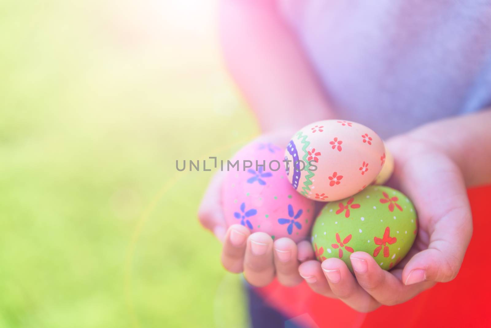 Happy easter! Close up of little kid holding colorful Easter eggs on green grass field background.