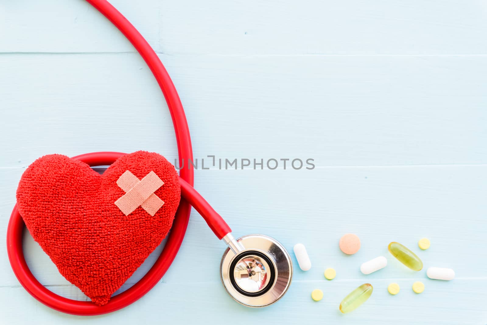 World health day, Healthcare and medical concept. Woman hand holding red heart with Stethoscope, notepad or notebook, thermometer and yellow Pill on Pastel white and blue wooden table background texture.