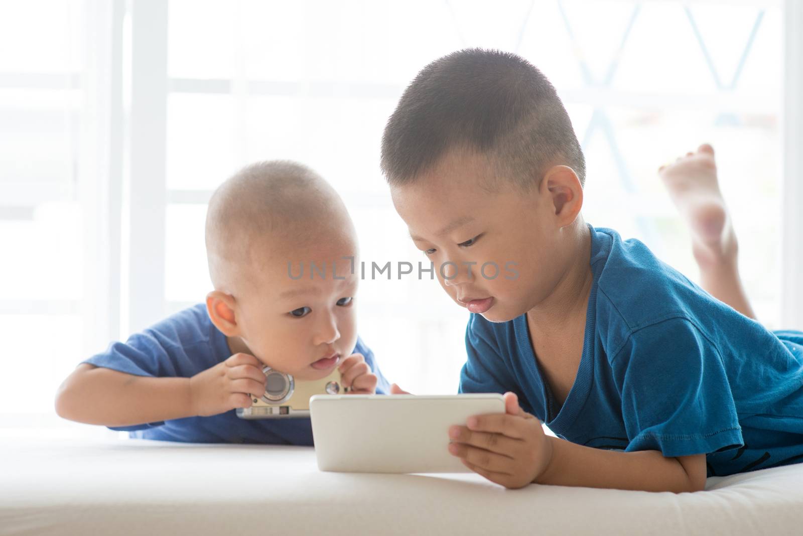 Young children addicted to technology gadget. Asian boys using smart phone at home.