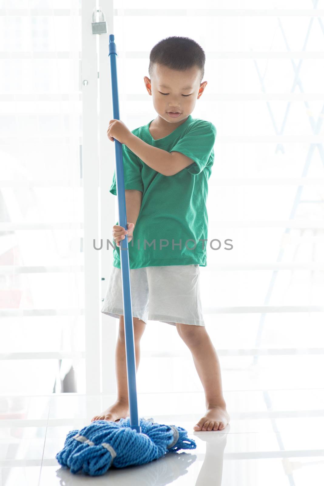 Asian boy mopping floor. Young child doing house chores at home.