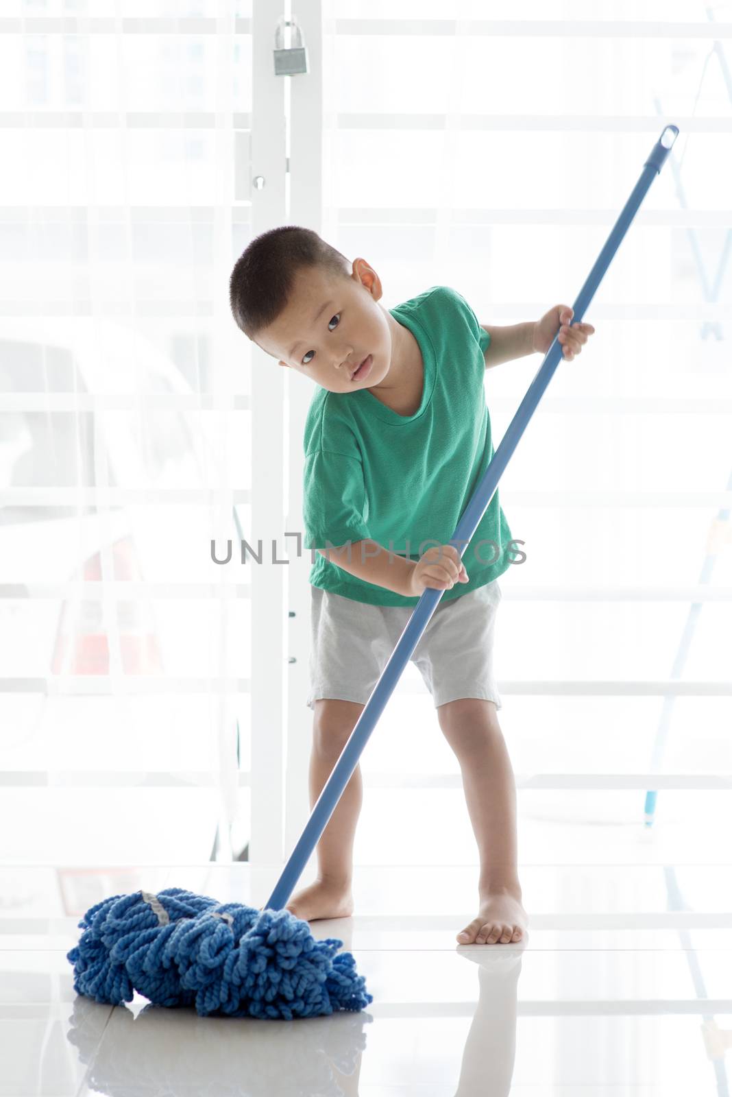 Asian boy cleaning floor with mop. Young child doing house chores at home.