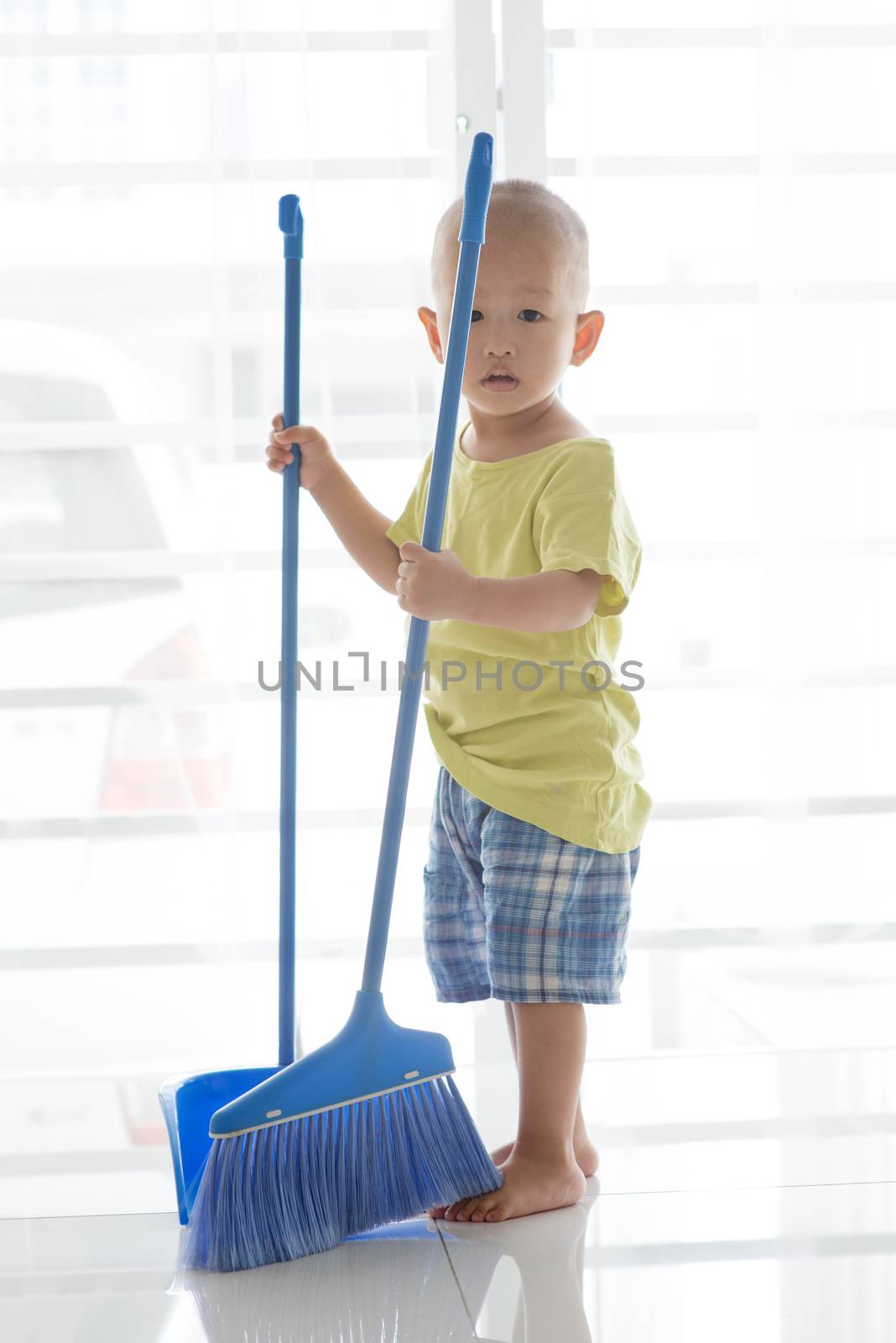 Asian toddler sweeping floor with broom. Young child doing house chores at home.