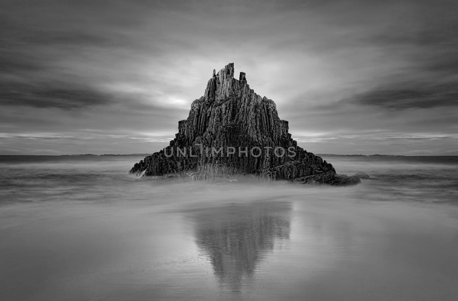 Moody sky over Pyramid Rock sea stack with tidal reflection.  Black and white