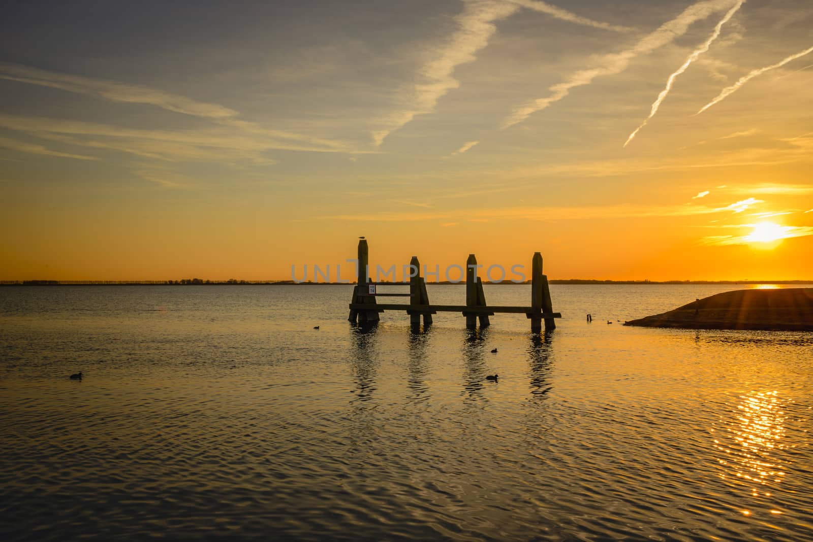 sunset in the northsea with lines from planes in the sky and wooden structure in the water