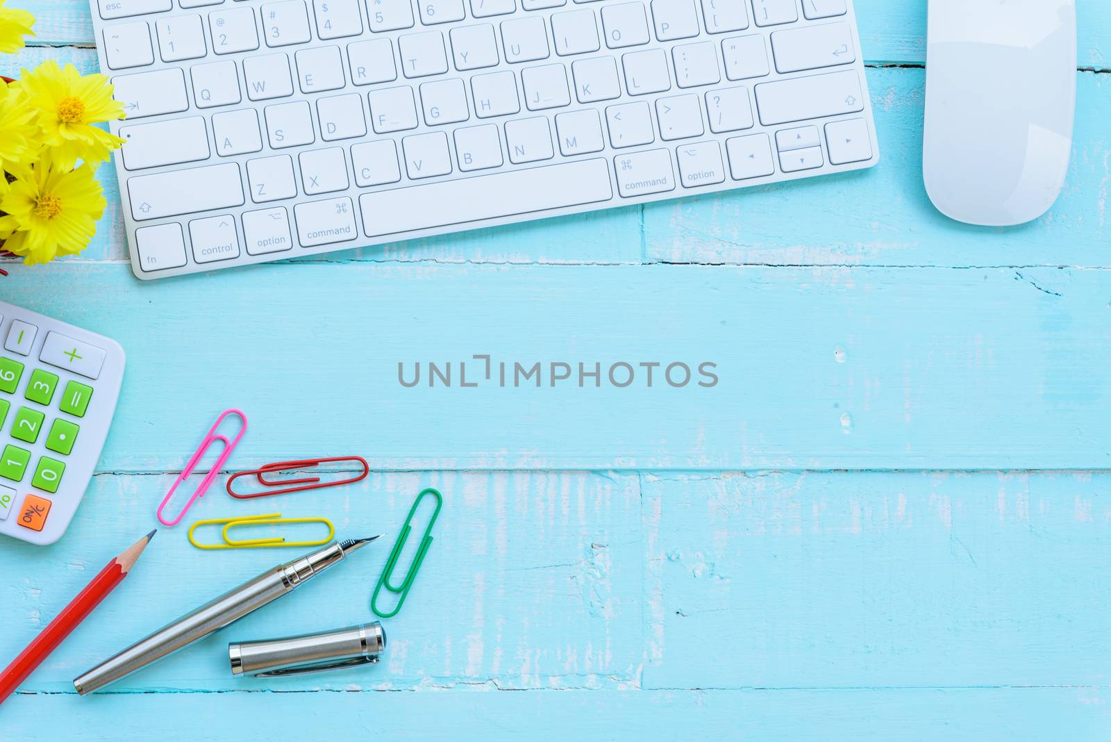 Top view office table with workspace and office accessories including calculator, mouse, keyboard, glasses, clips, flower, pen, pencil , note book and laptop on bright green wooden background.