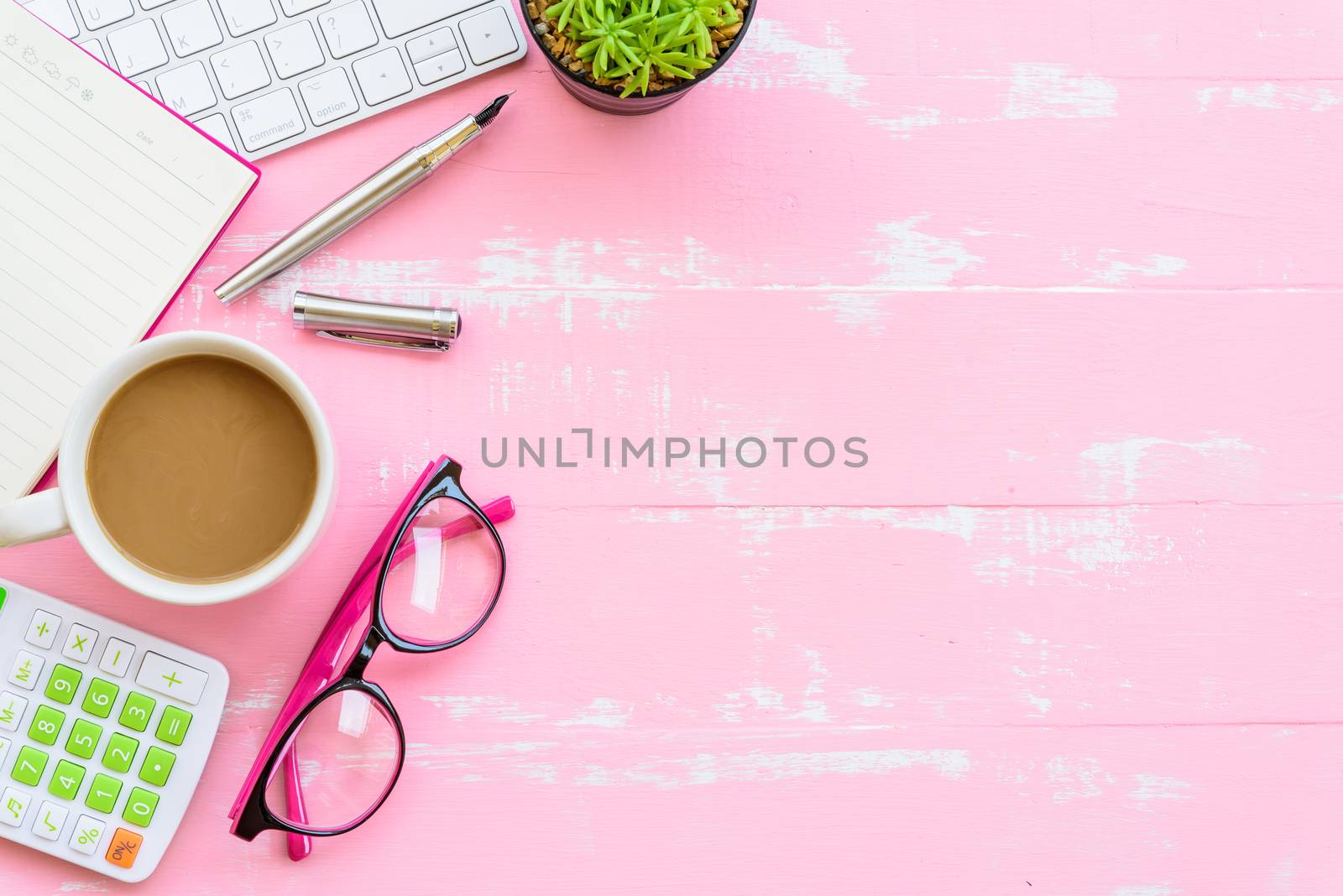 Top view office table with workspace and office accessories including calculator, mouse, keyboard, glasses, clips, flower, pen, pencil, note book, laptop and coffee on pink wooden background.