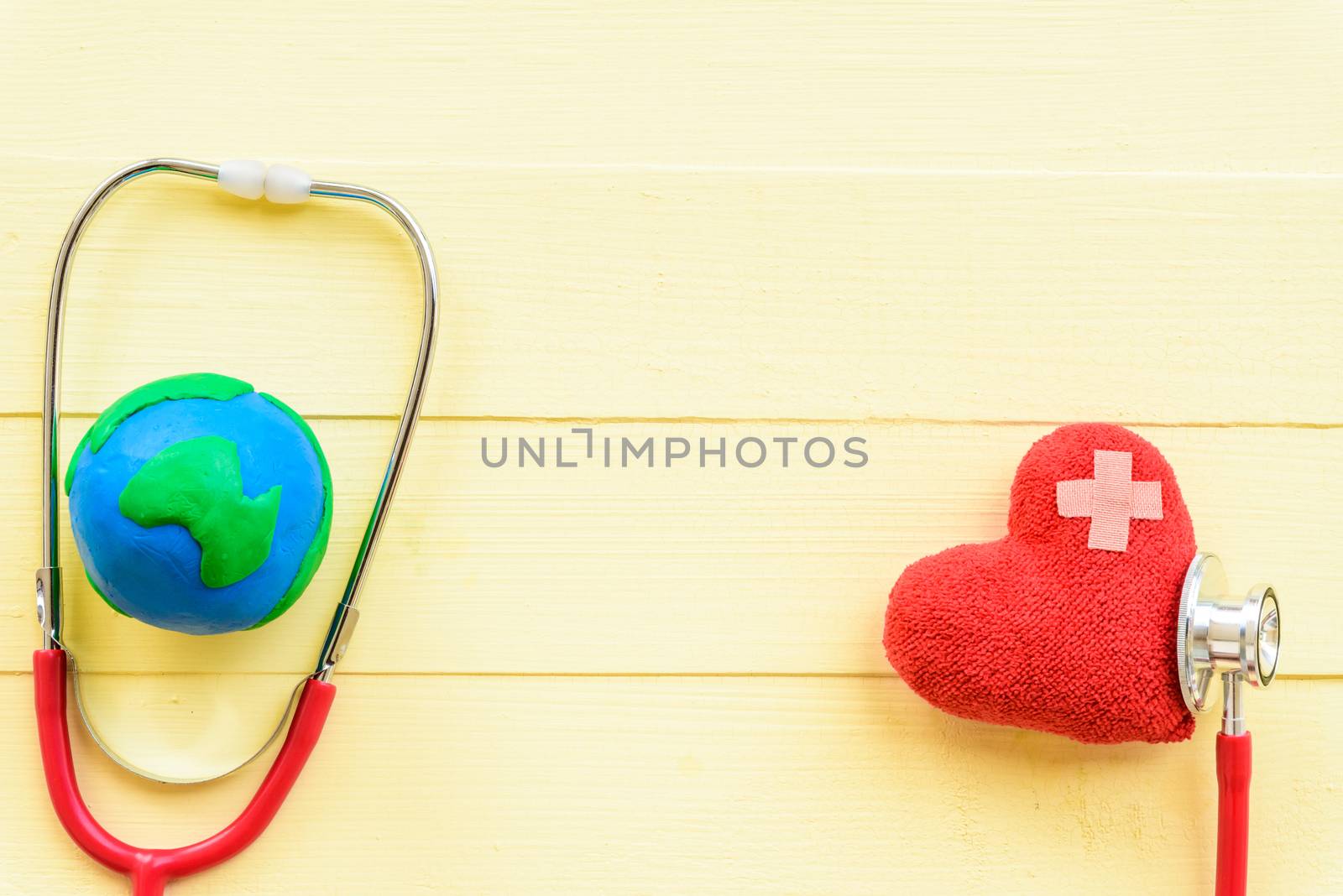 World health day, Healthcare and medical concept. Red heart with Stethoscope and handmade globe on Pastel white and yellow wooden background.