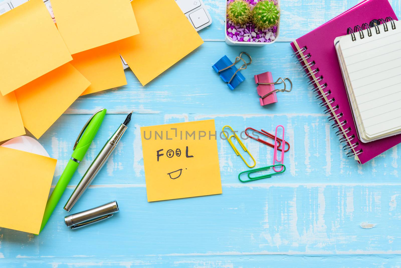 April fool's day celebration concept. office table with office accessories laptop, keyboard, mouse covered in sticky notes  on blue wooden background.