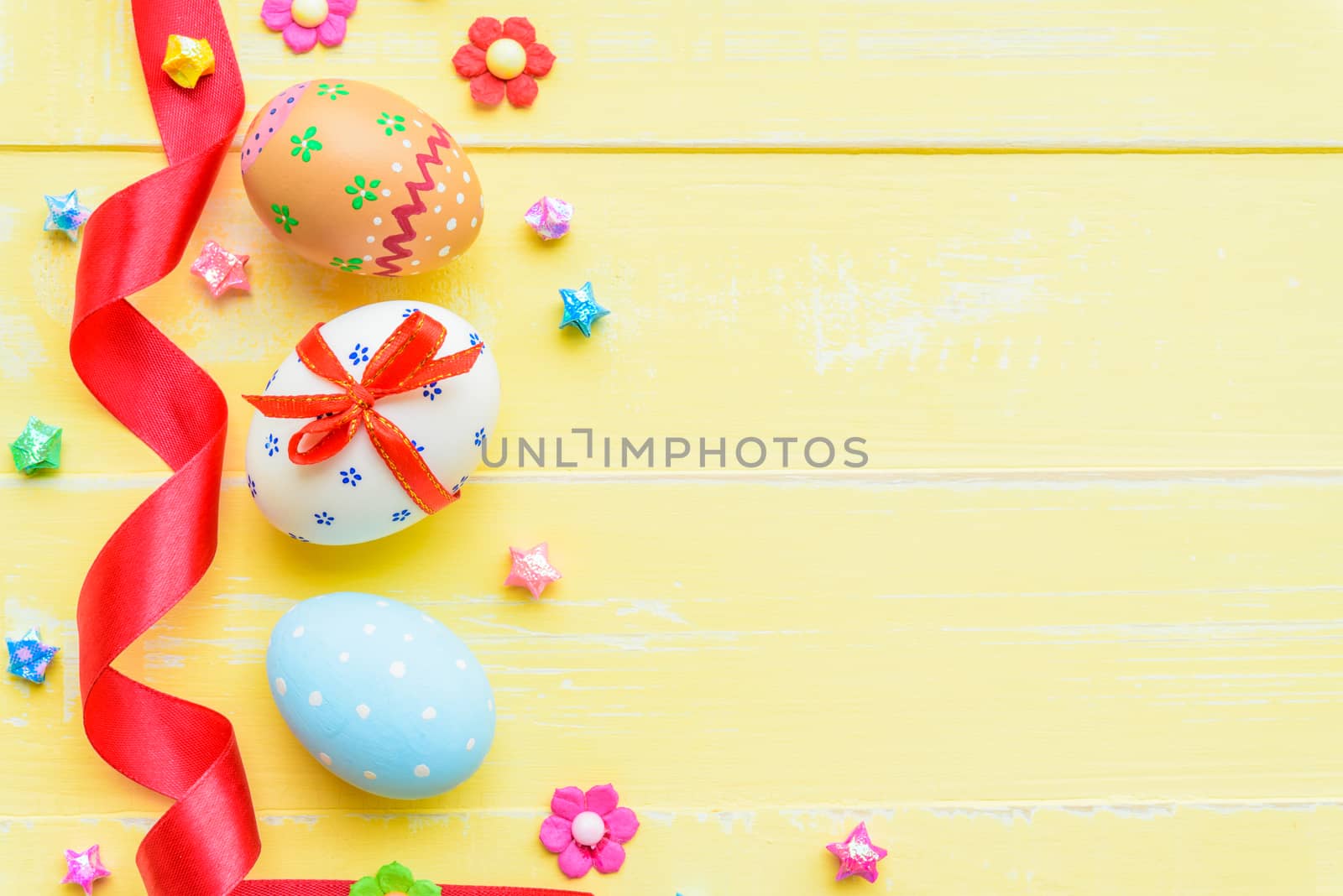 Happy easter! Colorful of Easter eggs in nest with red ribbon, Feather and paper star on pastel color bright yellow and white wooden background.