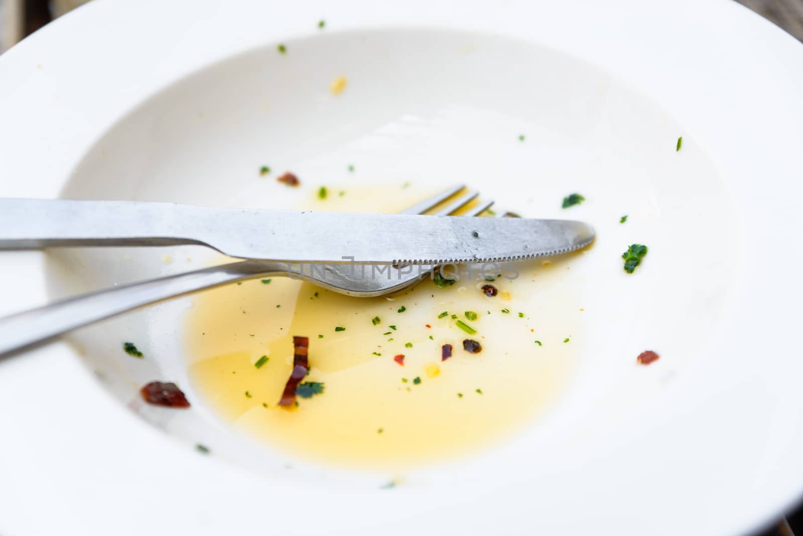 Empty white plate, knife and fork with olive oil, herbs and chili flakes leftover