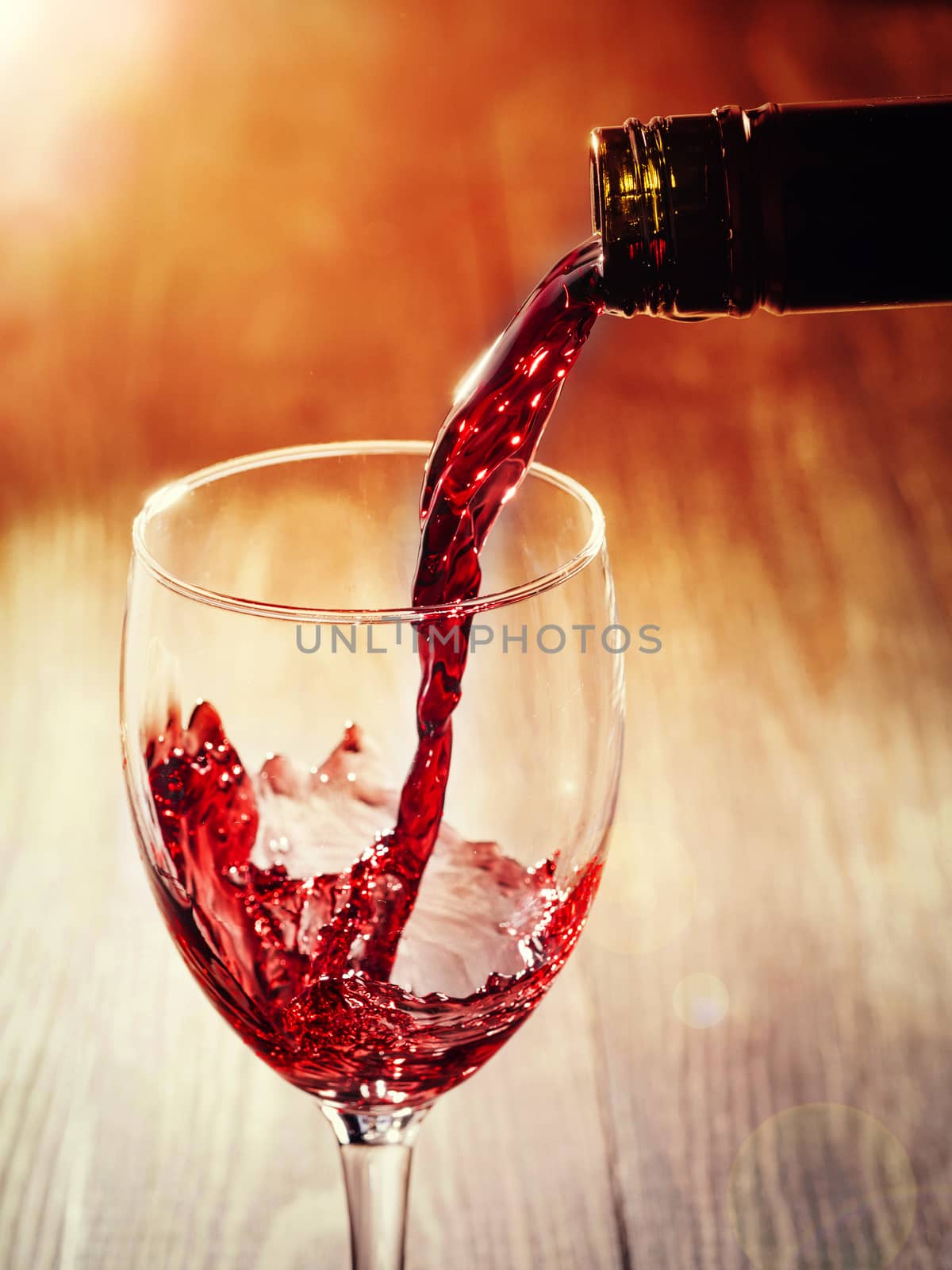 Closeup of red wine pouring in glass. Copy space. Sunflare effect
