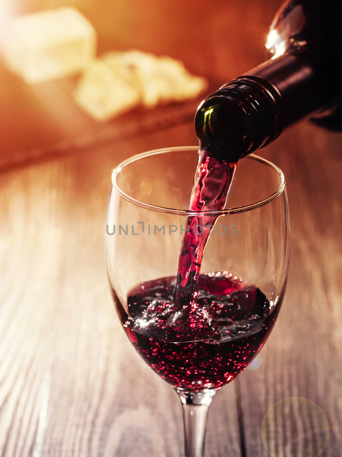 Closeup of red wine pouring in glass on wooden table. heese on background. Copy space. Sunflare effect