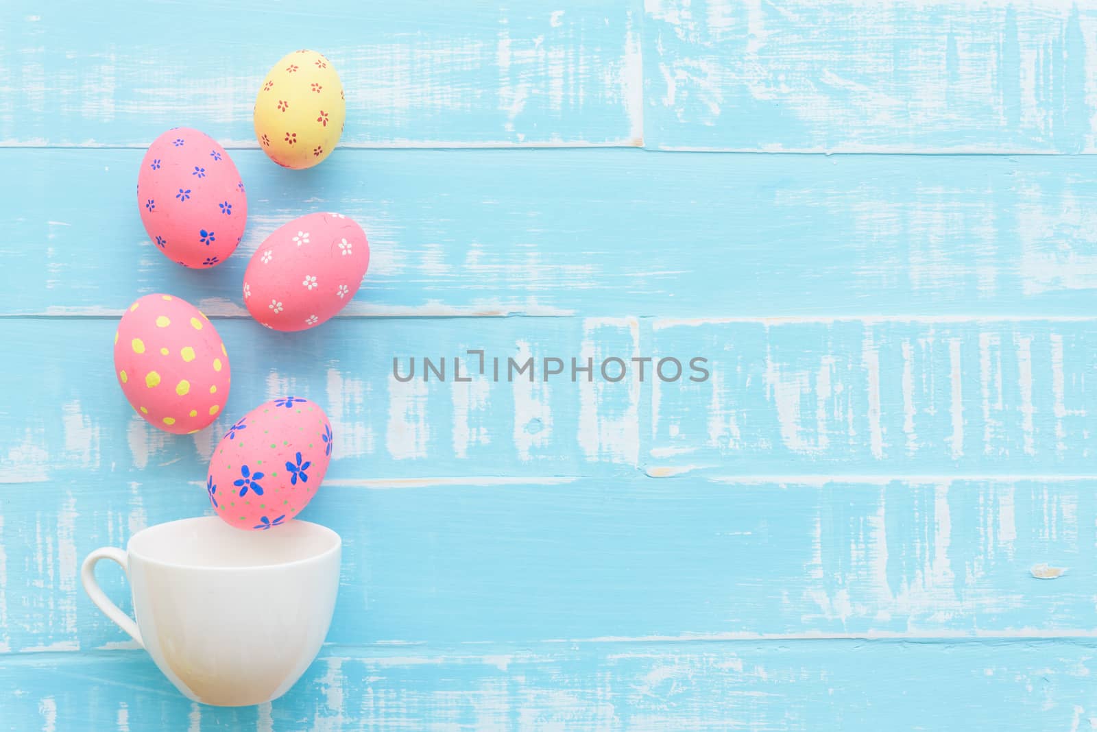 Happy easter! Row colorful Easter eggs spread out from white cup on bright green wooden background.