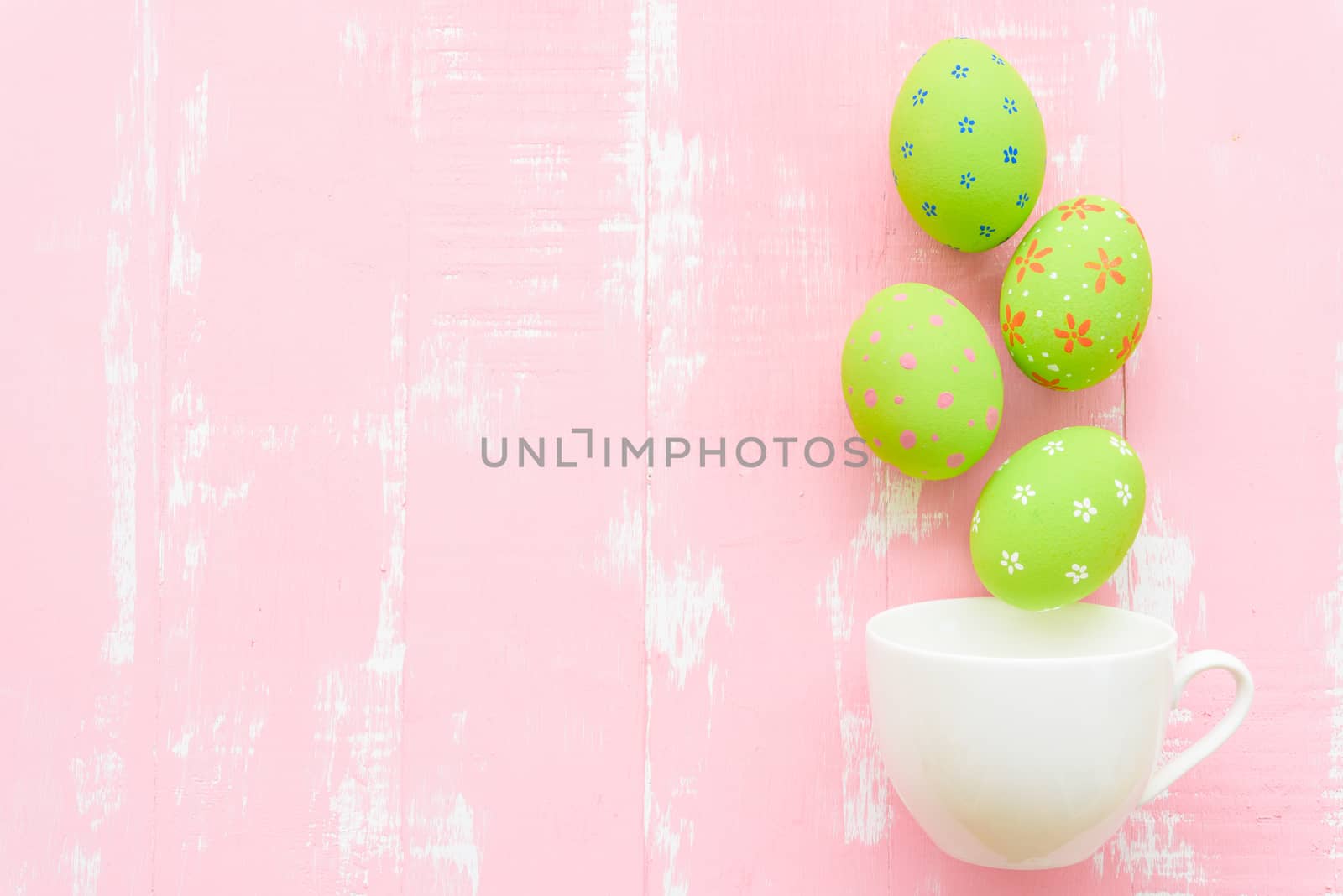 Happy easter! Row colorful Easter eggs spread out from white cup on bright pink and green wooden background.