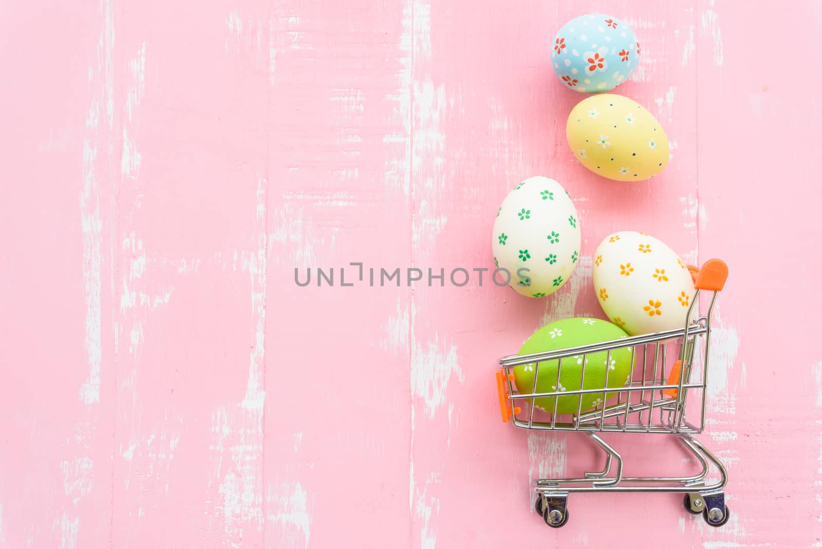 Happy easter! Row colorful Easter eggs spread out from shopping cart on bright pink wooden background.