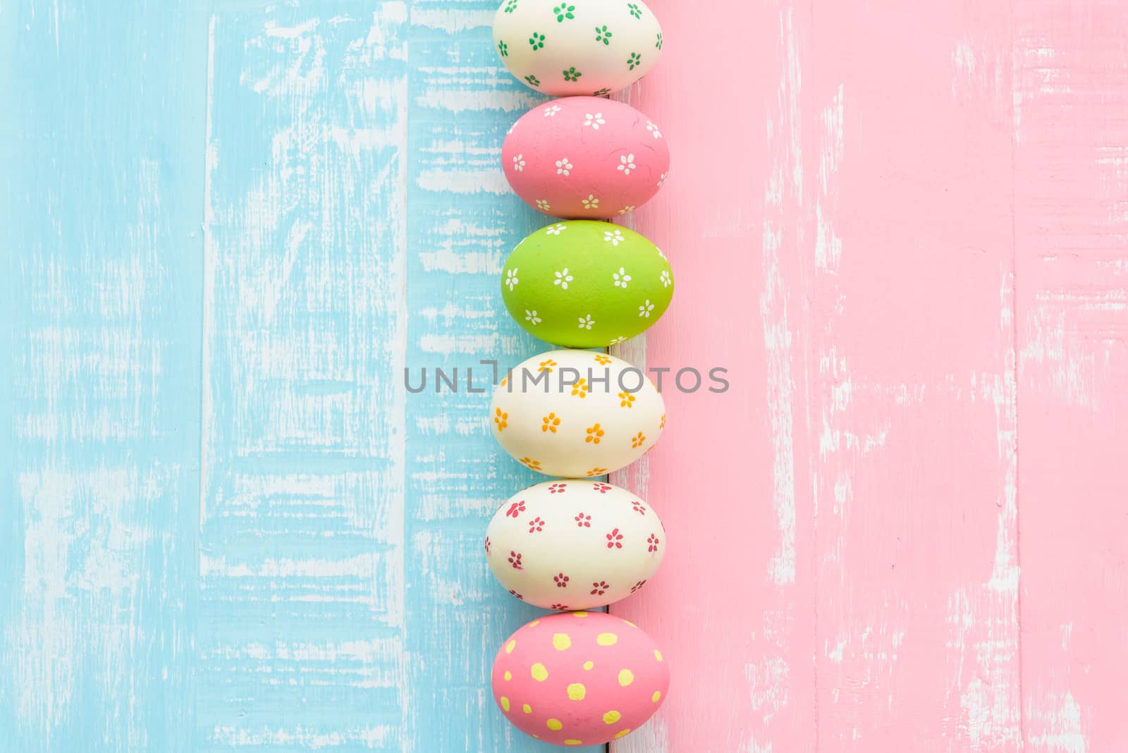 Happy easter! Row Easter eggs with colorful paper flowers on bright pink and green wooden background.