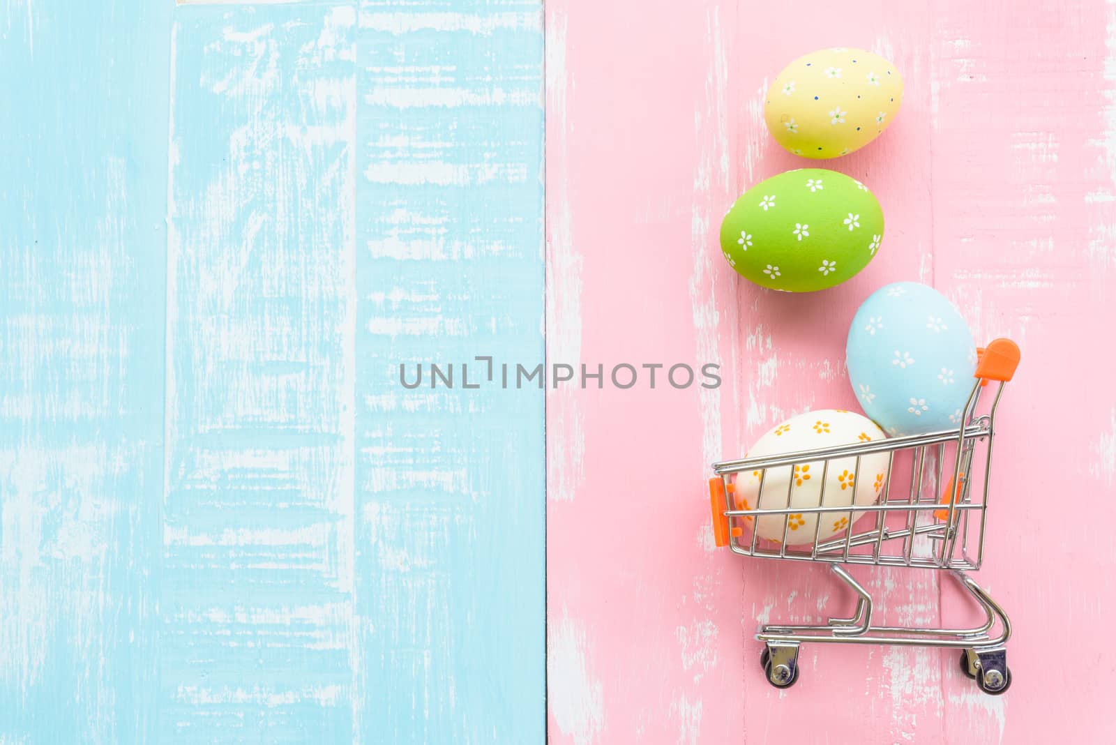 Happy easter! Row colorful Easter eggs spread out from shopping cart on bright pink and green wooden background.