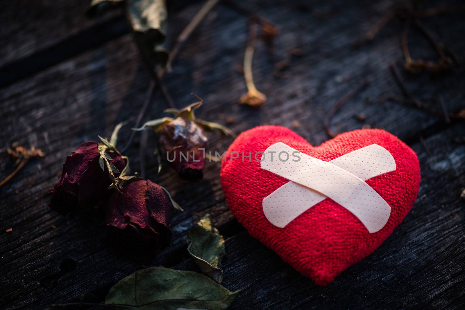 First Aid Band Cushioned Plaster Strip Medical Patch glued on red heart with dried red rose on wooden background. Heart broken, Love and Valentines day concept.