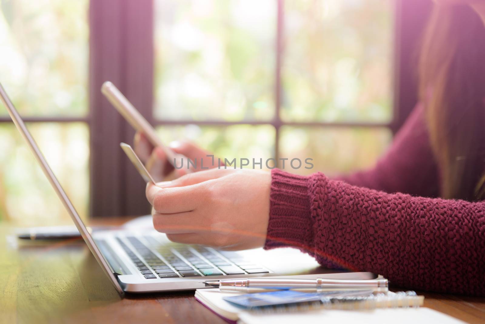 Pretty Young womans hands holding a credit card and using laptop computer for online shopping. Online payment. Female working on laptop in a cafe. Note book, pen and credit card put on table.