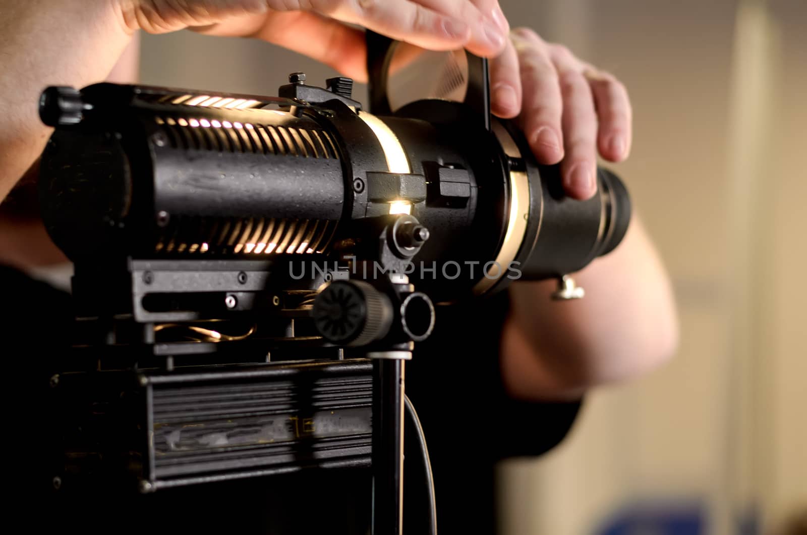 Man adjusts professional film spotlight bulb in studio. Precision lighting instruments in action.