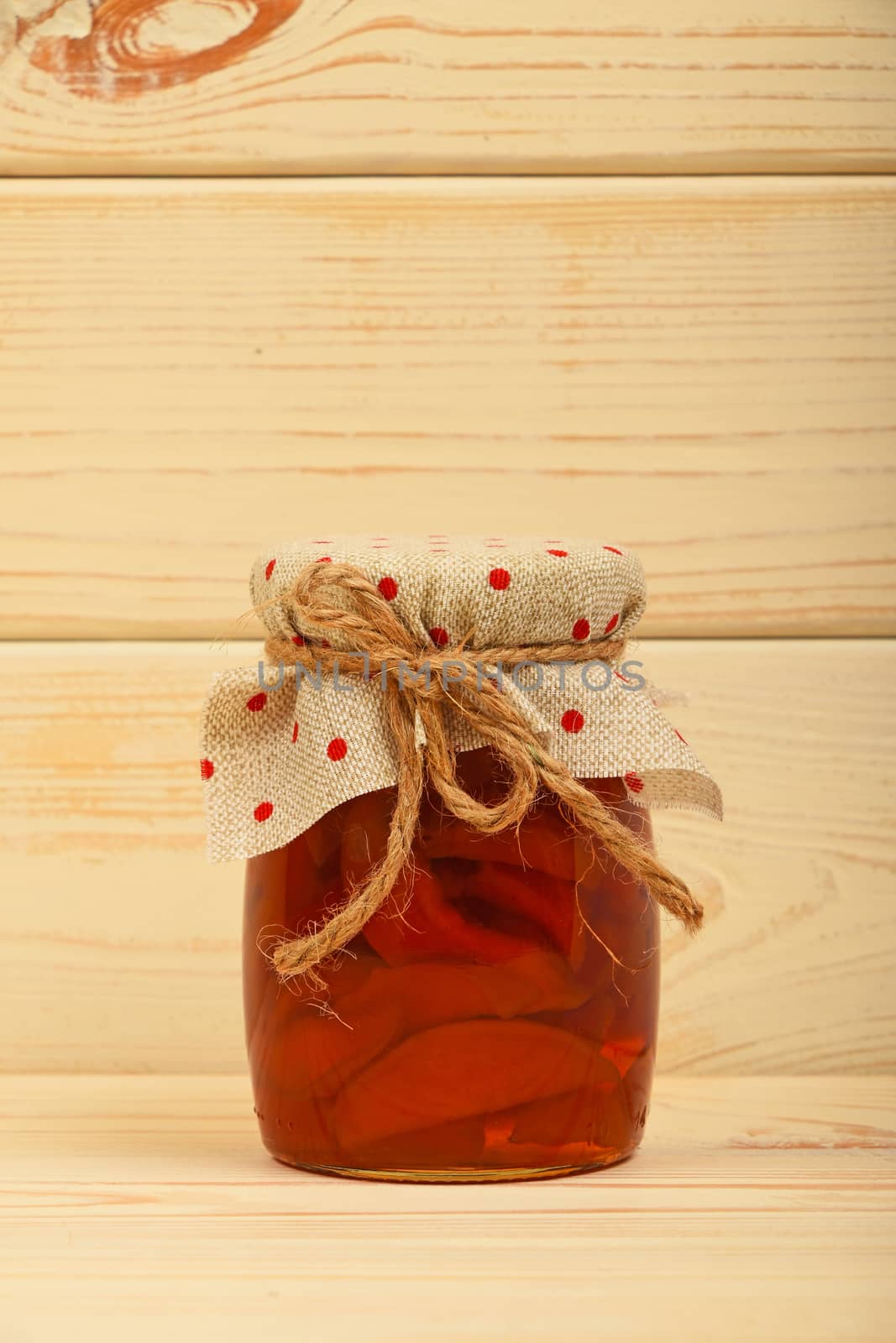 Close up of one glass jar of homemade quince jam with textile top decoration and twine bow over white beige painted vintage wooden planks background, low angle side view