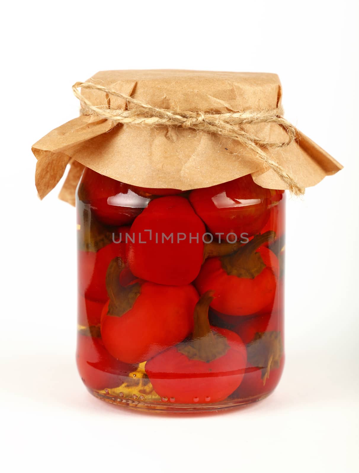 Close up of one glass jar of pickled small round red hot cherry chili peppers with kraft paper parchment decoration and twine over white background, low angle side view