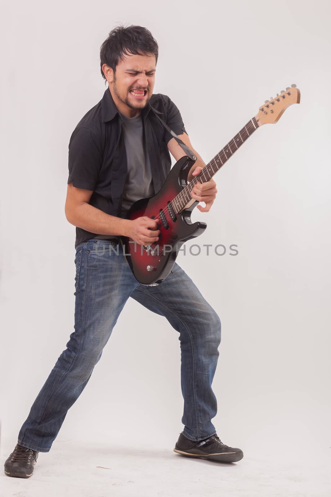 young man jumping with electric guitar on white background