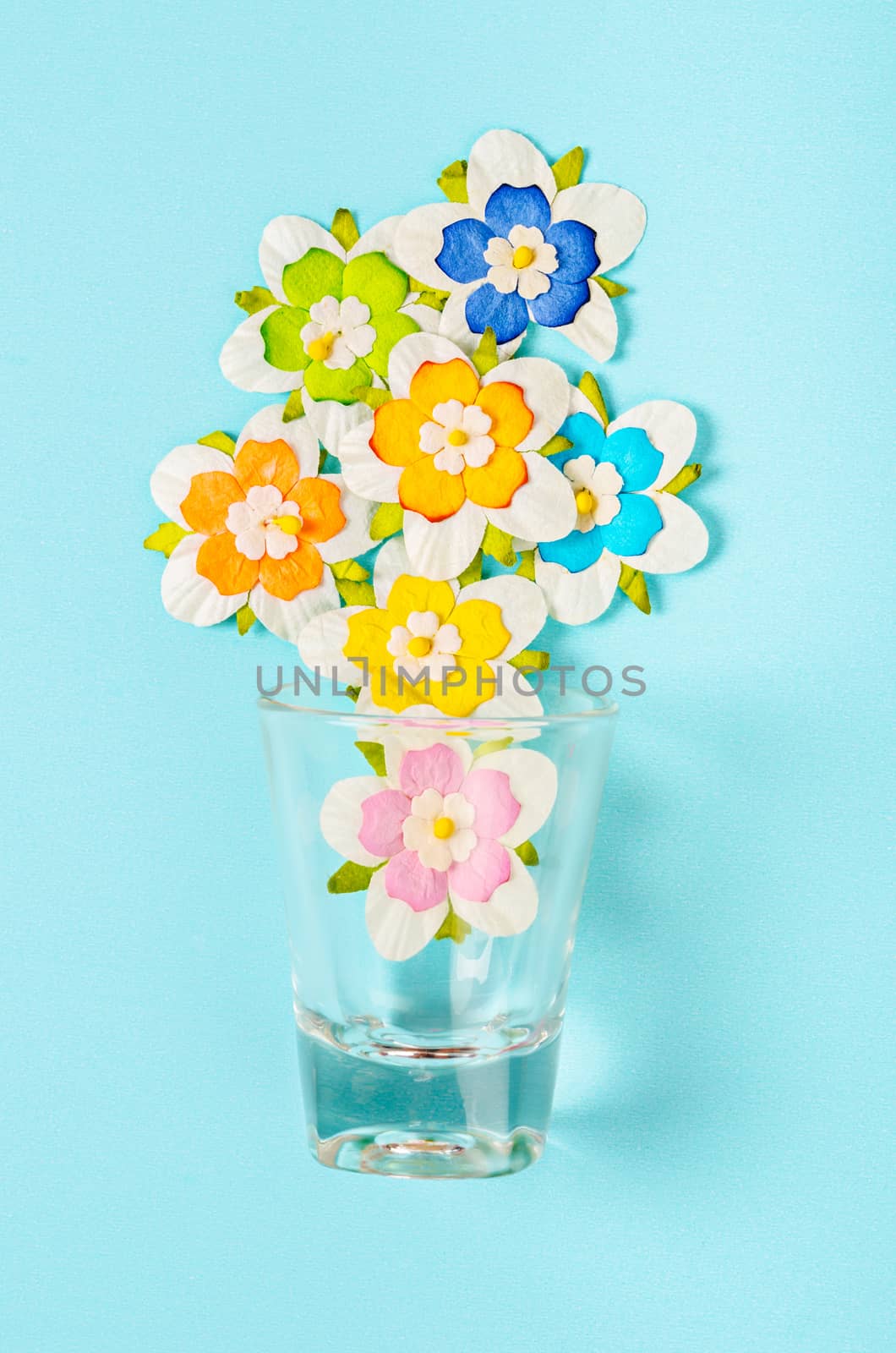 Romantic beautiful artificial colorful flowers with glass on blue background.