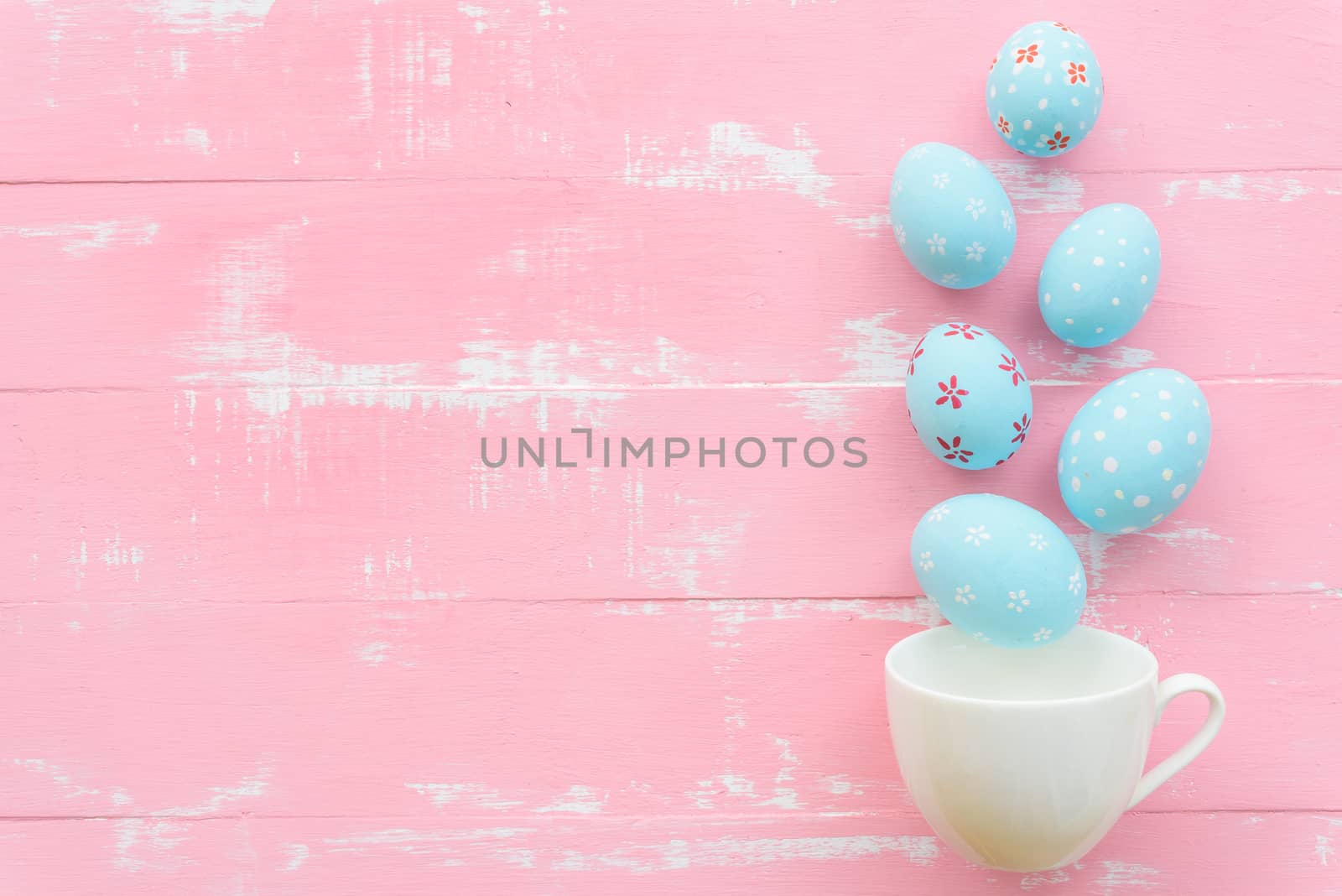 Happy easter! Row colorful Easter eggs spread out from white cup on bright pink and green wooden background.