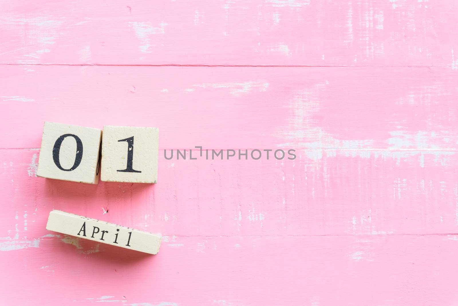 April Fools' Day concept. Wooden block calendar with empty space for text on bright pink and white wooden background.