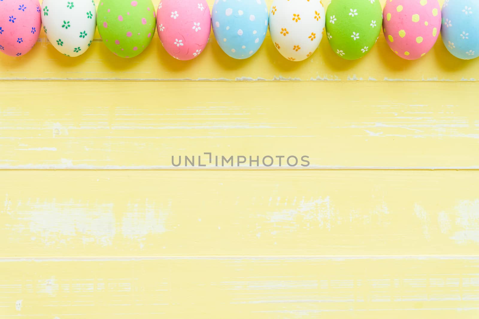 Happy easter! Row Easter eggs with colorful paper flowers on bright yellow wooden background.