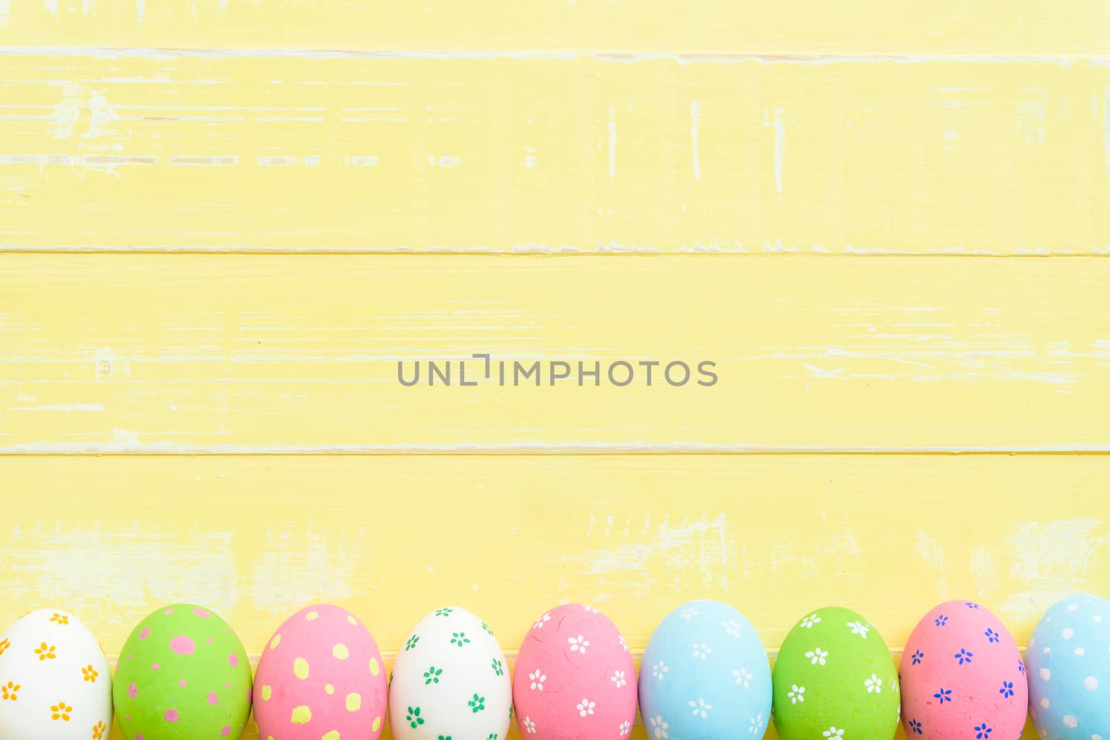 Happy easter! Row Easter eggs with colorful paper flowers on bright yellow wooden background.