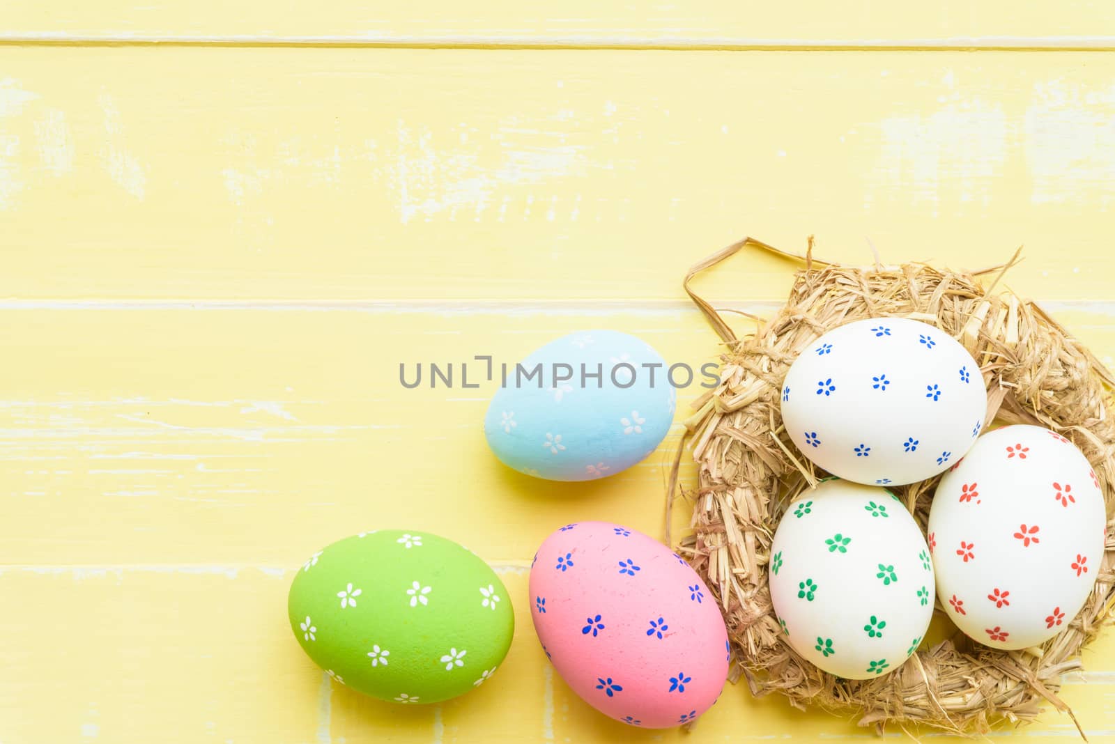 Happy easter! Colorful of Easter eggs in nest with red ribbon, Feather and paper star on pastel color bright yellow and white wooden background.