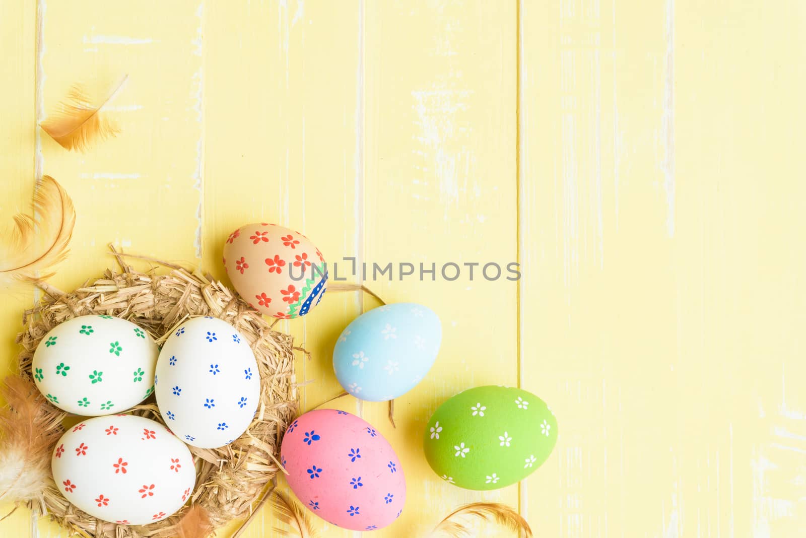 Happy easter! Colorful of Easter eggs in nest with red ribbon, Feather and paper star on pastel color bright yellow and white wooden background.