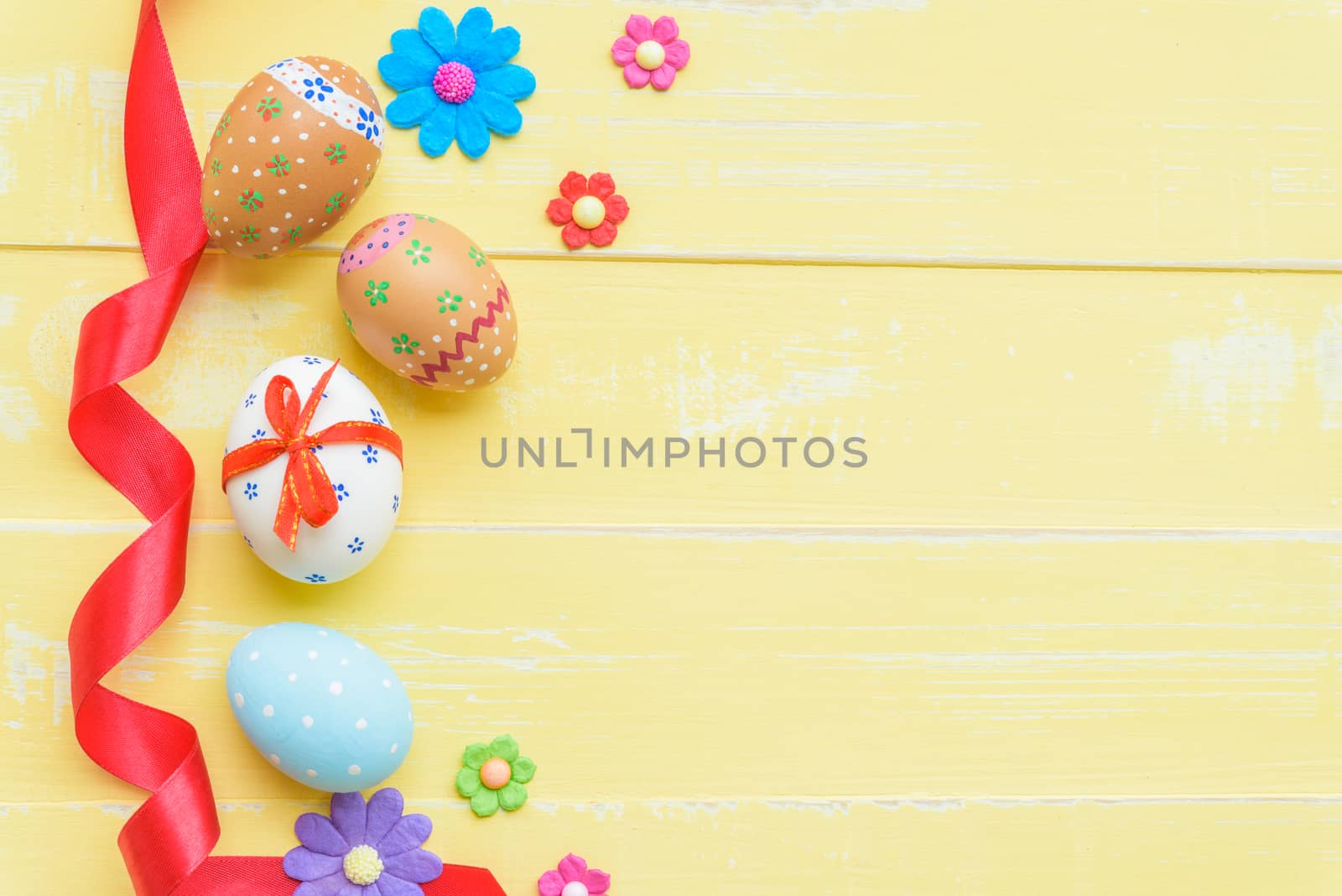 Happy easter! Colorful of Easter eggs in nest with red ribbon, Feather and paper star on pastel color bright yellow and white wooden background.