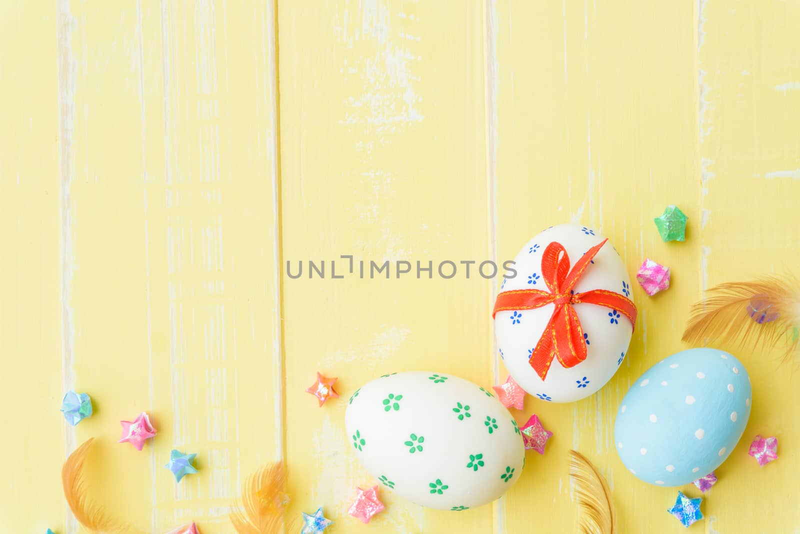 Happy easter! Colorful of Easter eggs in nest with red ribbon, Feather and paper star on pastel color bright yellow and white wooden background.
