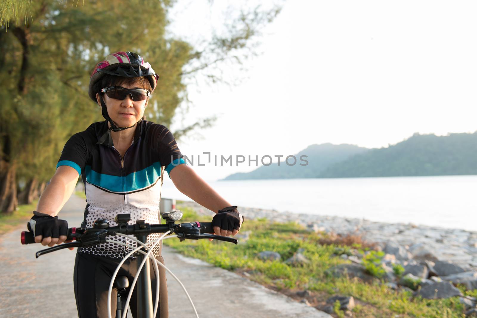 Joyful senior woman riding a bicycle by Kenishirotie