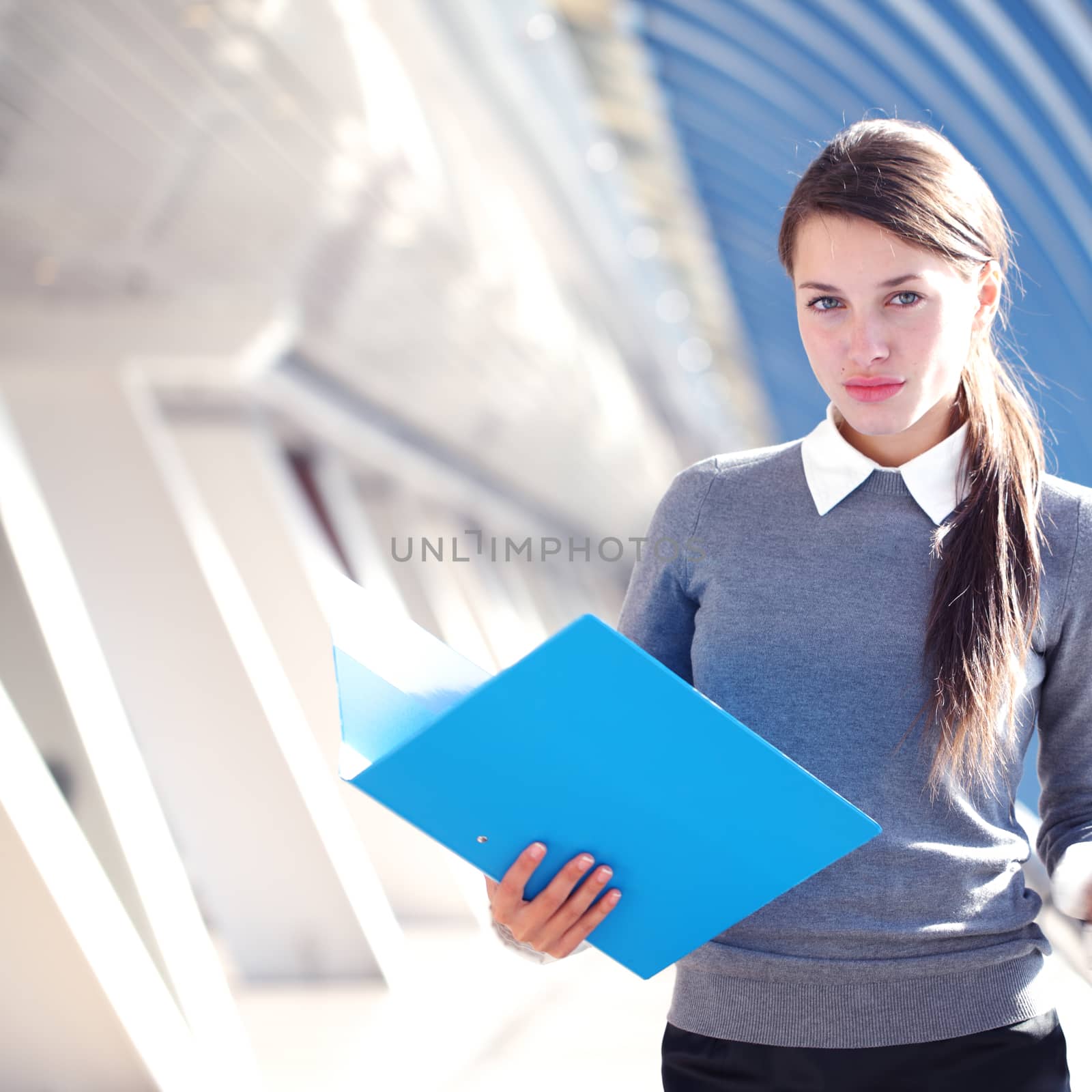 Young Businesswoman with folder standing in corridor of modern office building