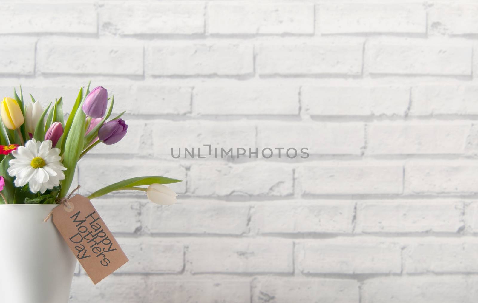 Selection of tulips and daisies inside a pot on top of a fireplace mantelpiece with label