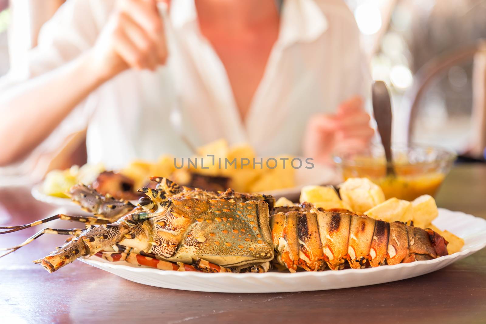 Lady on tropical vacations eating grilled lobster served with potatoes and coconut sauce.