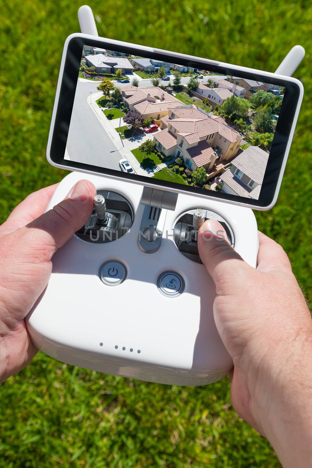 Hands Holding Drone Quadcopter Controller With Residential Homes on Screen.