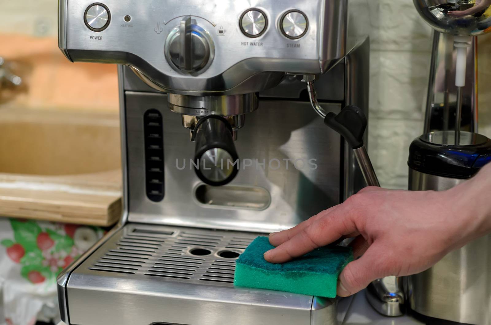 Barista cleaning coffee machine at cafe using green sponge