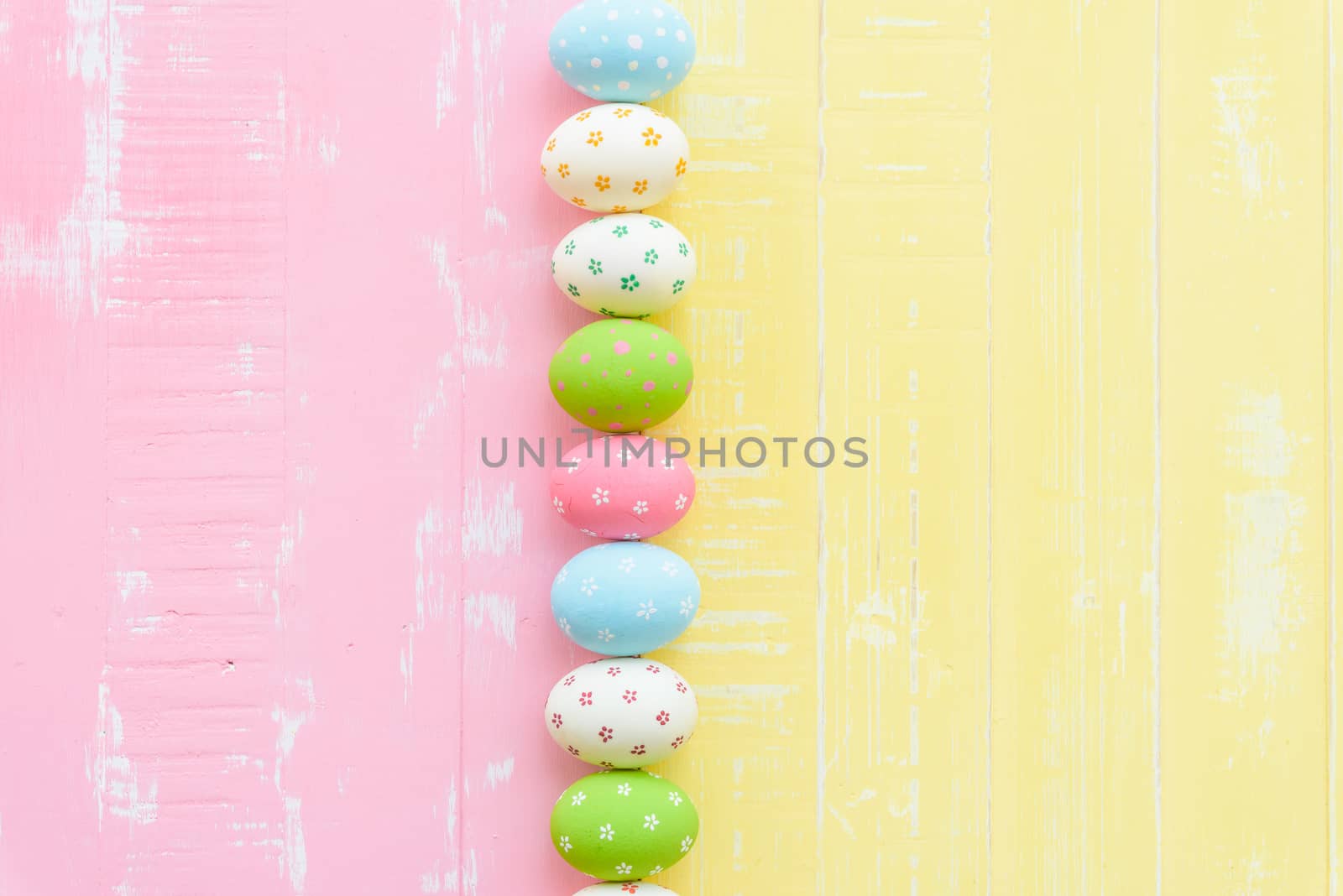 Happy easter! Row Easter eggs with colorful paper flowers on bright pink and yellow wooden background.