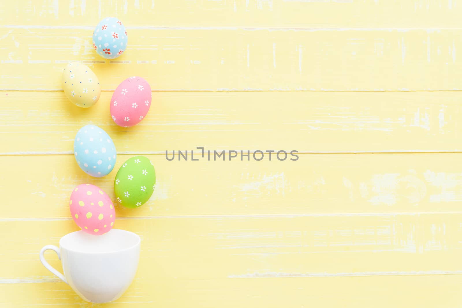 Happy easter! Row colorful Easter eggs spread out from white cup on bright yellow wooden background.