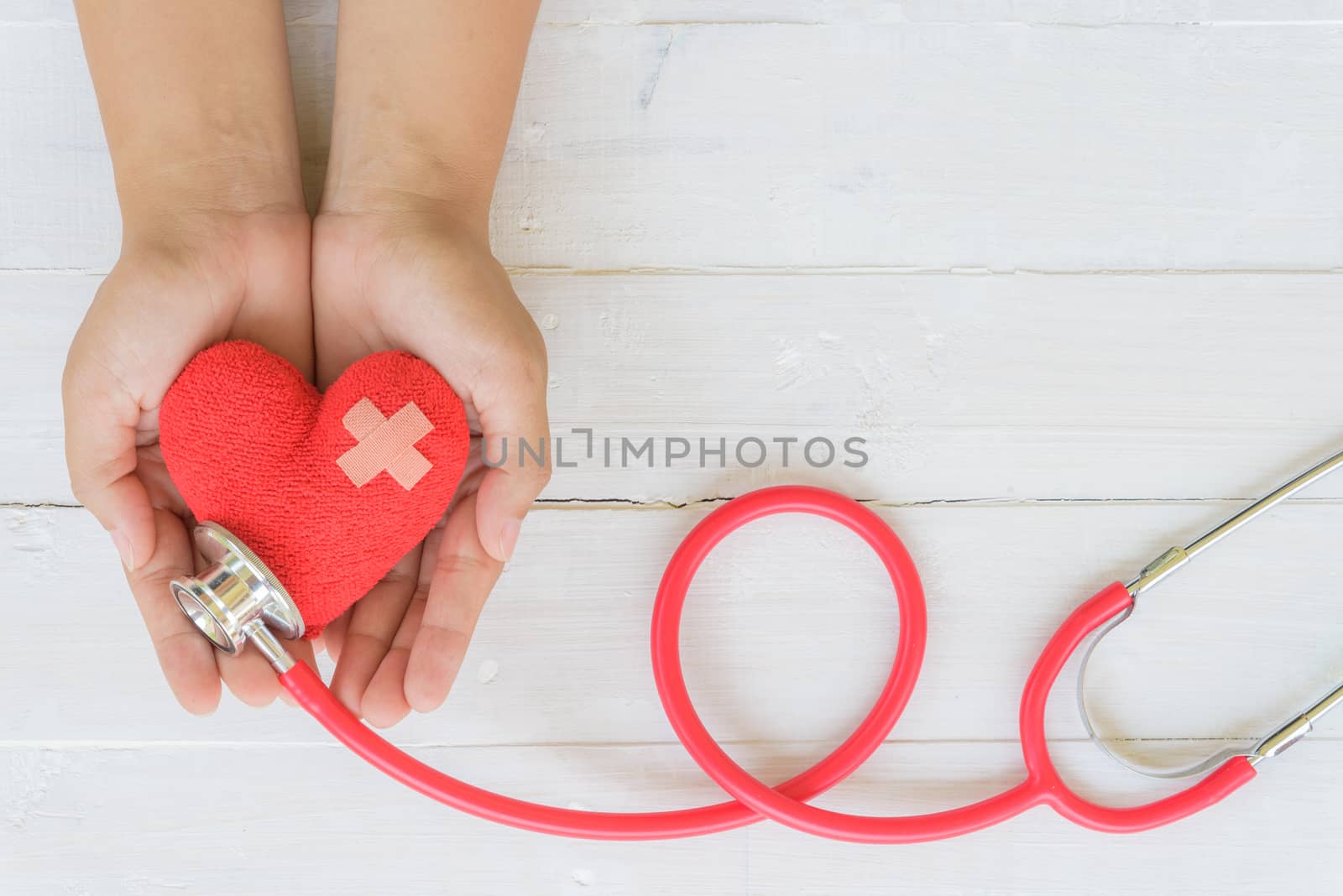 World health day, Healthcare and medical concept. Woman hand holding red heart with Stethoscope, notepad or notebook, thermometer and yellow Pill on Pastel white and blue wooden table background texture.