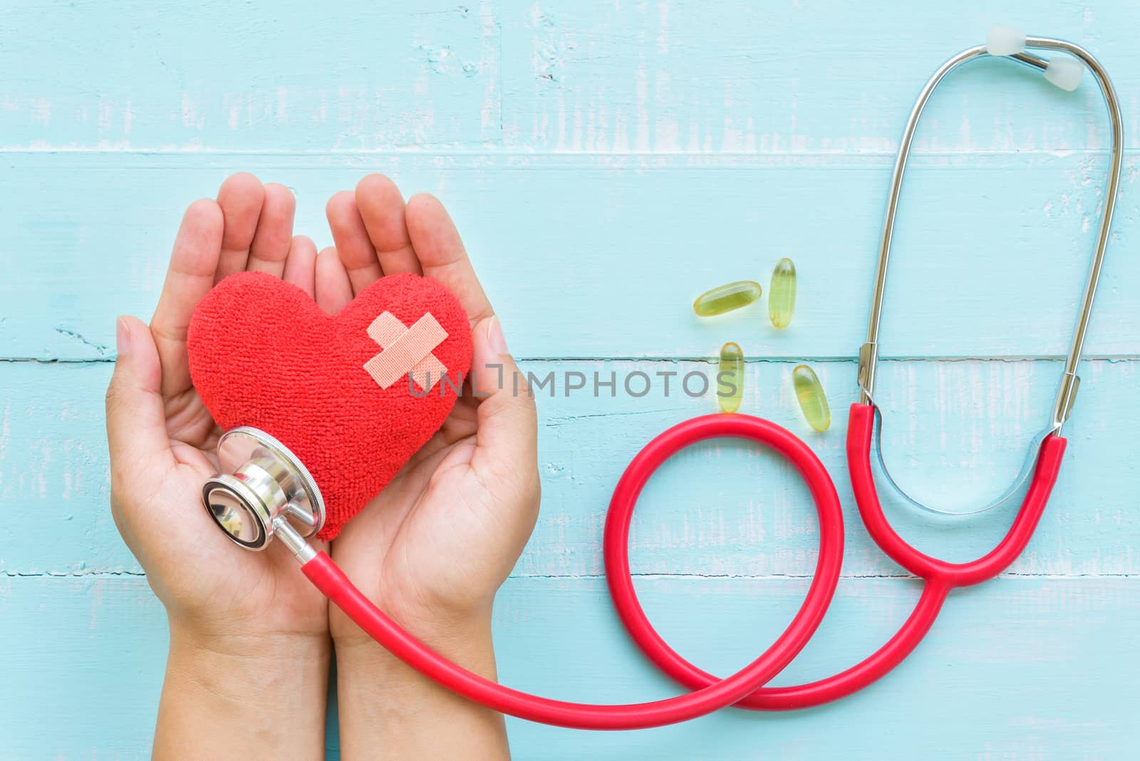 World health day, Healthcare and medical concept. Woman hand holding red heart with Stethoscope, notepad or notebook, thermometer and yellow Pill on Pastel white and blue wooden table background texture.