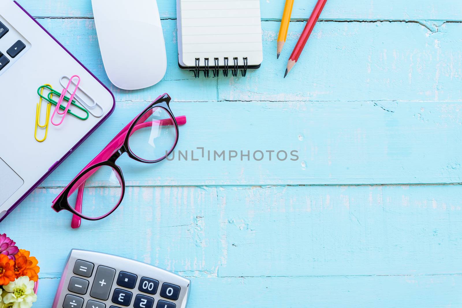 Top view office table with workspace and office accessories including calculator, mouse, keyboard, glasses, clips, flower, pen, pencil , note book and laptop on bright green wooden background.