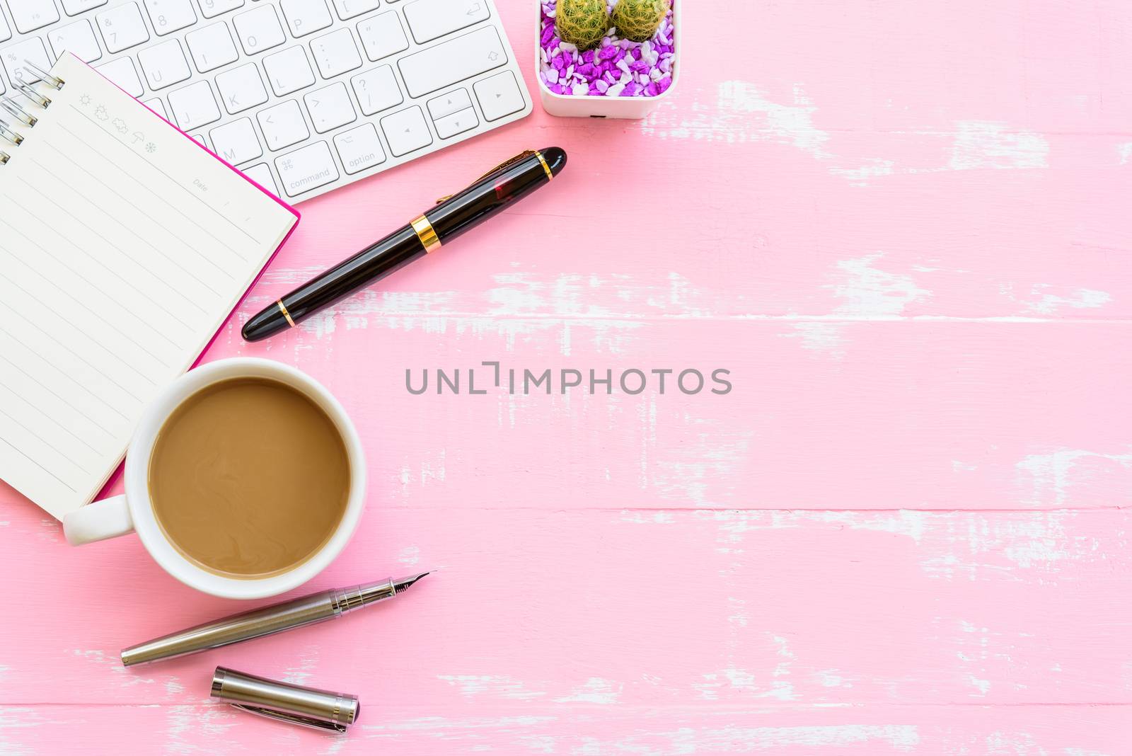 Top view office table with workspace and office accessories including calculator, mouse, keyboard, glasses, clips, flower, pen, pencil, note book, laptop and coffee on pink wooden background.