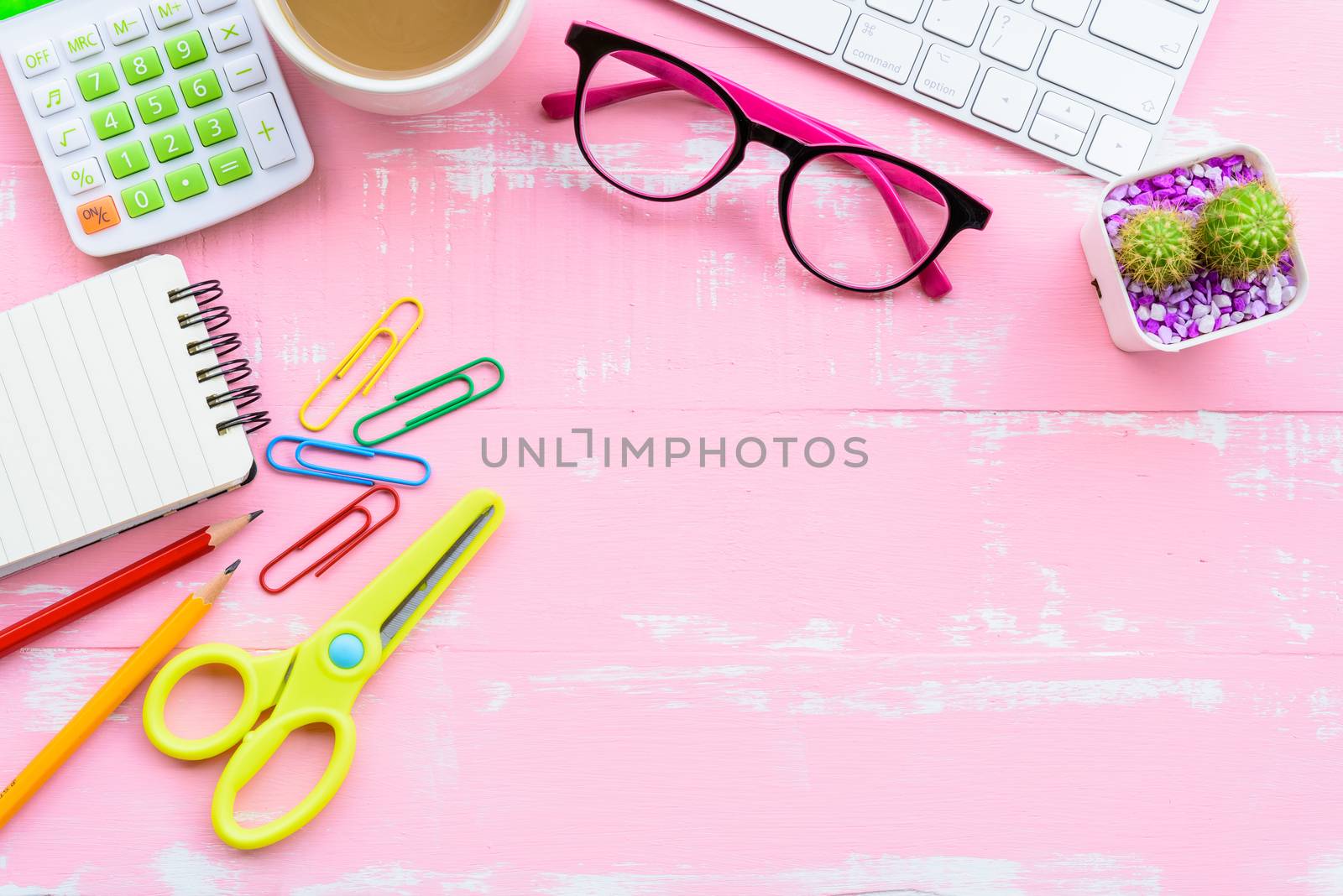Top view office table with workspace and office accessories including calculator, mouse, keyboard, glasses, clips, flower, pen, pencil, note book, laptop and coffee on pink wooden background.