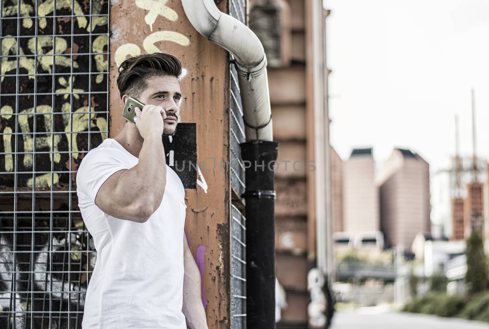 Handsome young man standing outdoors in urban environment on metal stairs, talking on cell phone